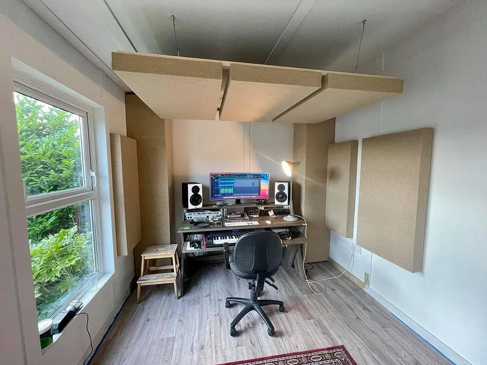 Habitación pequeña con un gran panel suspendido del techo sobre el escritorio y paneles en las paredes, junto a una ventana con vegetación exterior.